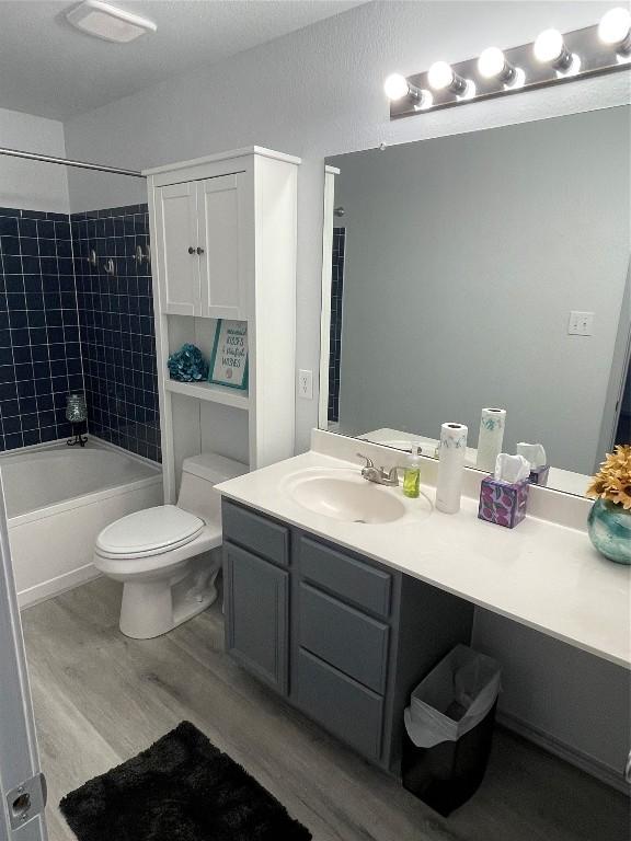 full bathroom with vanity, hardwood / wood-style floors, toilet, and tiled shower / bath