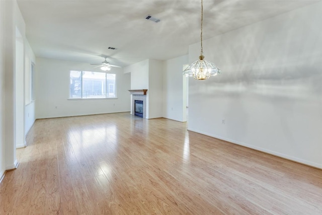 unfurnished living room featuring ceiling fan with notable chandelier, light hardwood / wood-style floors, and a tile fireplace