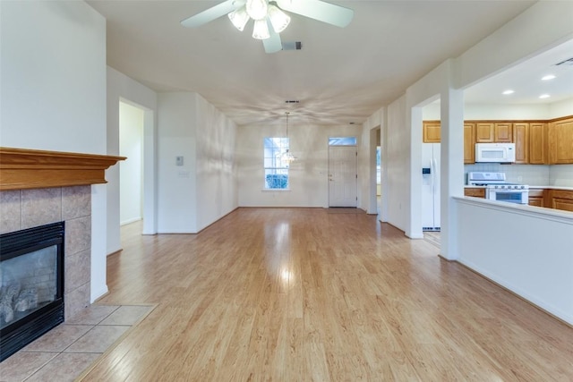 unfurnished living room with a tile fireplace, ceiling fan, and light wood-type flooring