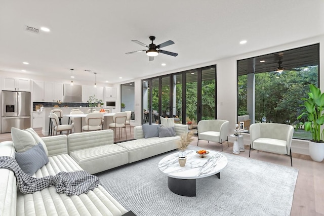 living room featuring expansive windows, ceiling fan, and light wood-type flooring