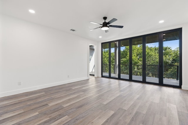 spare room featuring ceiling fan, a wall of windows, and light wood-type flooring