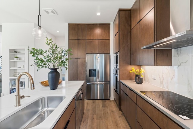 kitchen featuring stainless steel appliances, light countertops, a sink, modern cabinets, and wall chimney exhaust hood