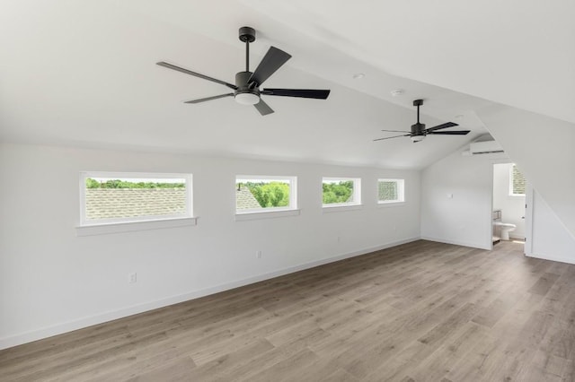 empty room featuring light wood finished floors, baseboards, ceiling fan, vaulted ceiling, and a wall mounted AC