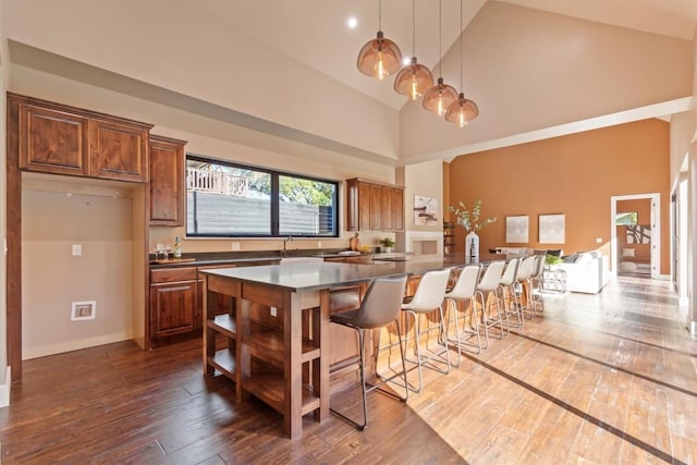 kitchen featuring dark wood-type flooring, a breakfast bar area, decorative light fixtures, a center island, and high vaulted ceiling