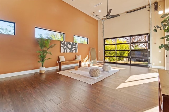 workout area with ceiling fan, a towering ceiling, and hardwood / wood-style floors