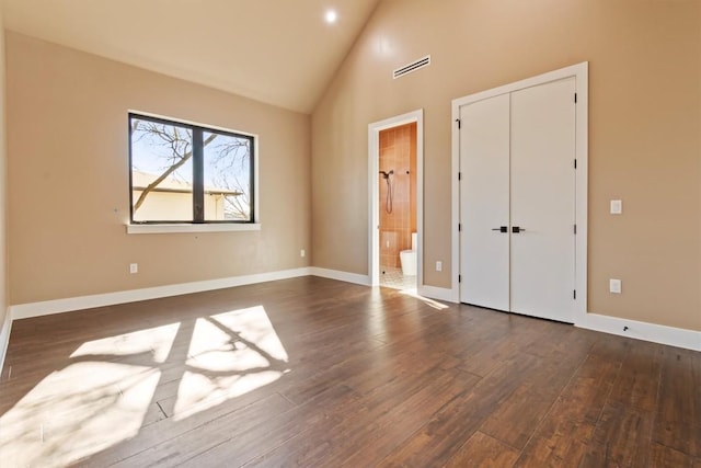 unfurnished bedroom featuring dark hardwood / wood-style floors, connected bathroom, high vaulted ceiling, and a closet