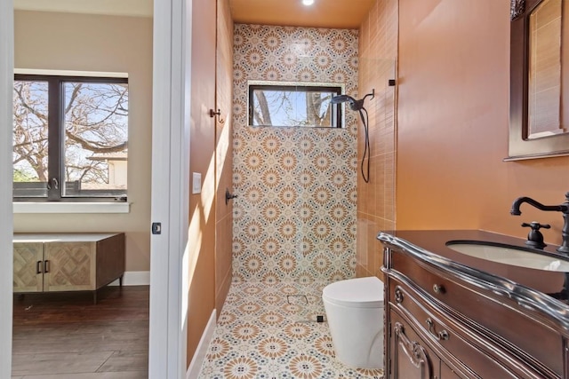 bathroom with hardwood / wood-style flooring, tiled shower, vanity, and toilet