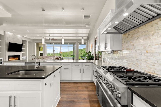 kitchen with wall chimney exhaust hood, high end range, decorative light fixtures, a fireplace, and white cabinets