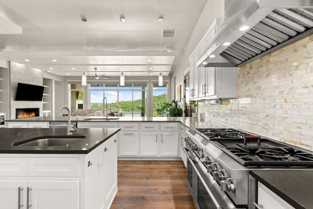 821 Laughing Dog Ct, Leander, TX 78641 - kitchen featuring wall chimney exhaust hood, high end range, open floor plan, dark countertops, and dark wood-type flooring