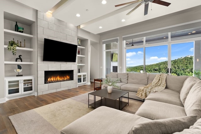 living room with ceiling fan, dark hardwood / wood-style floors, a fireplace, built in shelves, and beamed ceiling