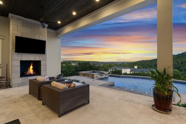 pool at dusk with a fireplace, an in ground hot tub, and a patio area