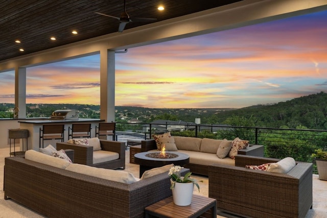 patio terrace at dusk featuring grilling area, an outdoor living space with a fire pit, and ceiling fan