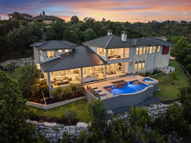 back house at dusk with a patio, an outdoor living space, pool water feature, a balcony, and an in ground hot tub