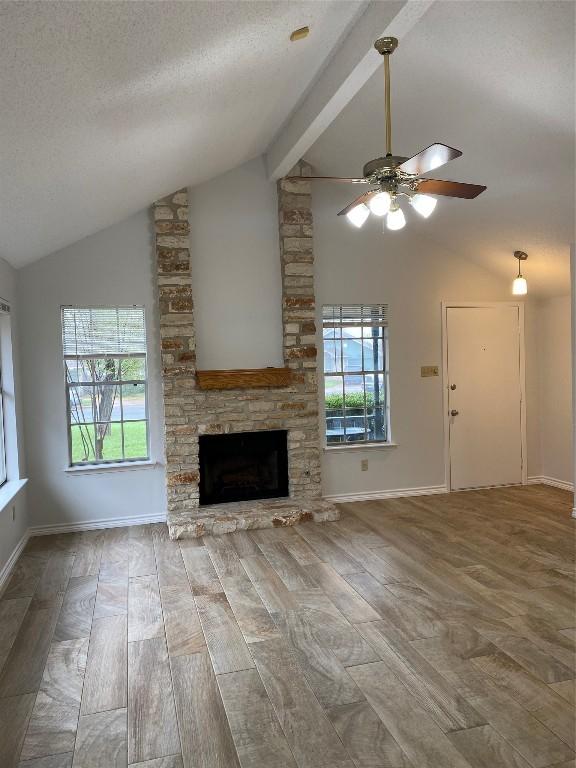 unfurnished living room with beamed ceiling, wood-type flooring, a stone fireplace, and a textured ceiling