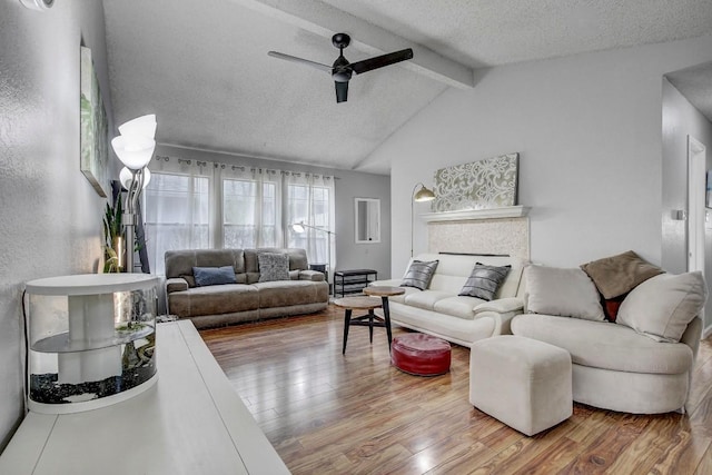 living room featuring wood-type flooring, lofted ceiling with beams, a textured ceiling, ceiling fan, and a fireplace