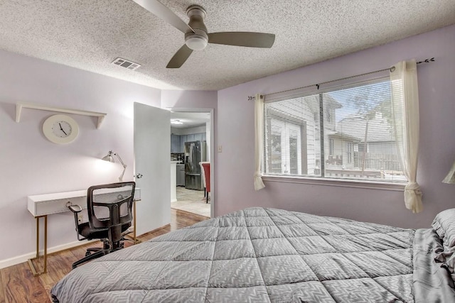 bedroom with ceiling fan, stainless steel fridge, light hardwood / wood-style floors, and a textured ceiling