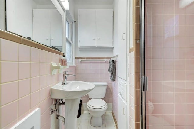 bathroom with tile walls, a shower with shower door, tile patterned floors, and toilet