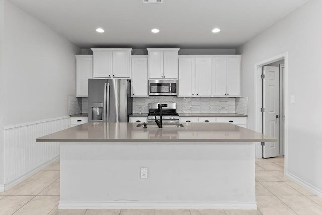 kitchen featuring a wainscoted wall, a kitchen island with sink, a sink, appliances with stainless steel finishes, and white cabinetry