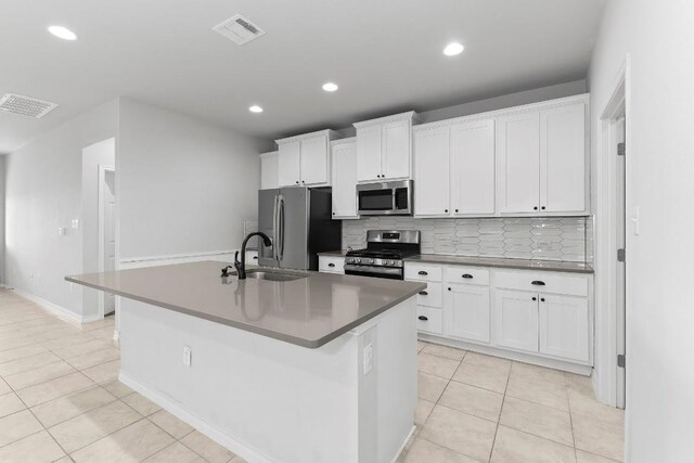 kitchen featuring sink, light tile patterned floors, appliances with stainless steel finishes, a kitchen island with sink, and white cabinetry