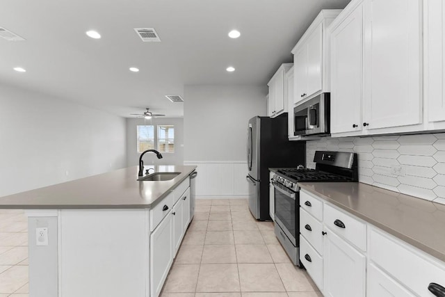 kitchen featuring visible vents, a wainscoted wall, an island with sink, appliances with stainless steel finishes, and a sink