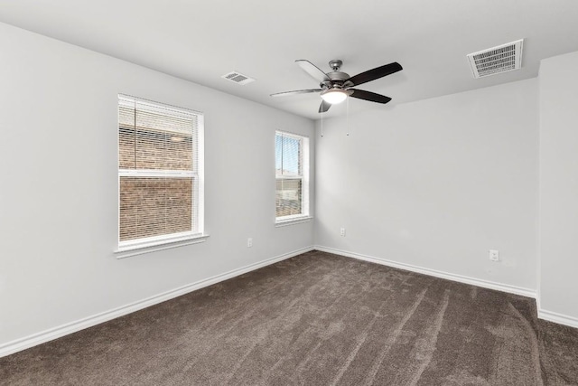 spare room featuring dark colored carpet, visible vents, baseboards, and a ceiling fan