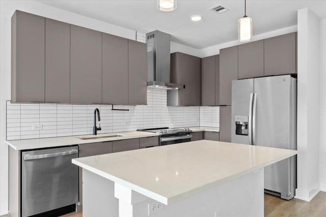 kitchen featuring a kitchen island, decorative light fixtures, sink, stainless steel appliances, and wall chimney range hood