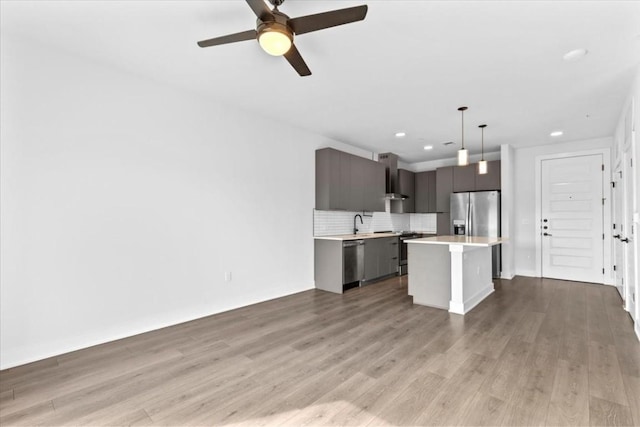 kitchen featuring appliances with stainless steel finishes, a center island, light hardwood / wood-style floors, decorative light fixtures, and wall chimney exhaust hood