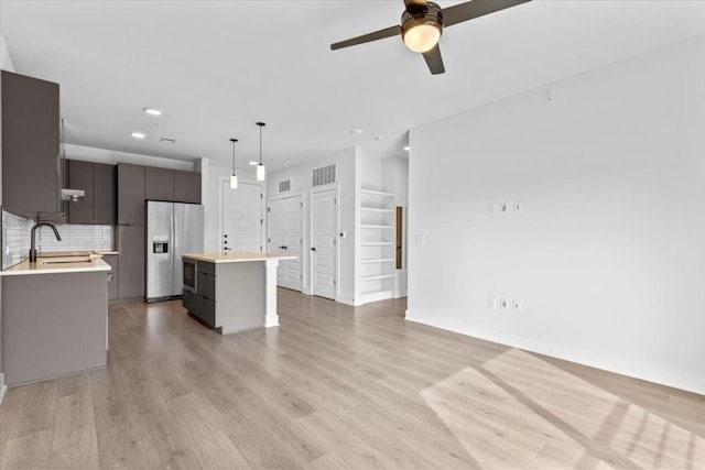 kitchen with a kitchen island, pendant lighting, sink, stainless steel fridge, and light wood-type flooring