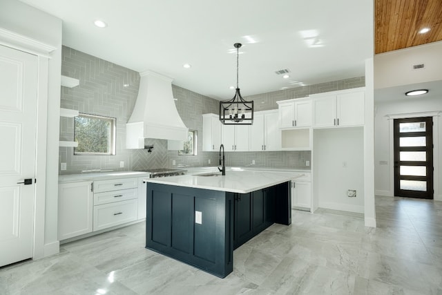 kitchen featuring white cabinetry, premium range hood, sink, and a center island with sink