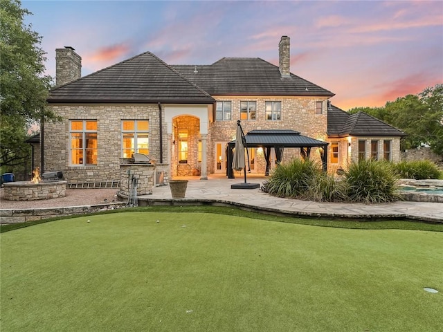 back house at dusk with a gazebo, a patio, and an outdoor fire pit