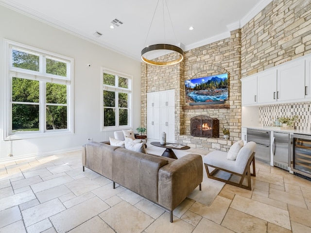 living room featuring crown molding, a towering ceiling, wine cooler, a fireplace, and bar area