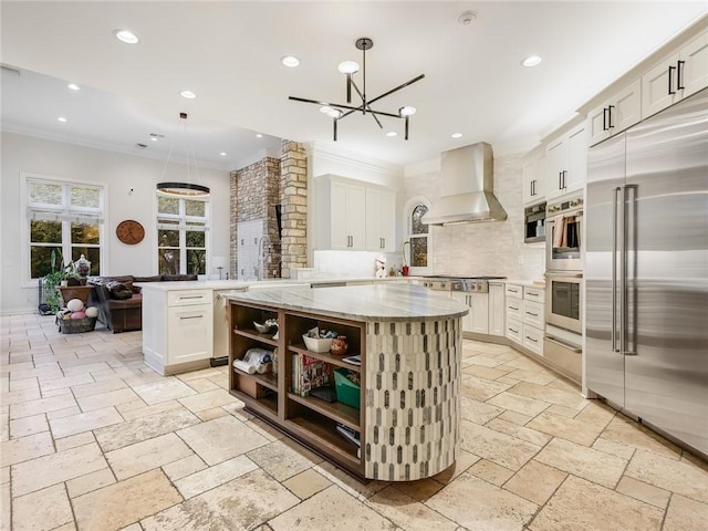 3844 Hunterwood Pt, Austin, TX 78746 - kitchen featuring wall chimney exhaust hood, appliances with stainless steel finishes, crown molding, backsplash, and stone tile flooring