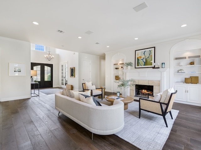 living room with crown molding, dark wood-type flooring, a fireplace, built in shelves, and french doors