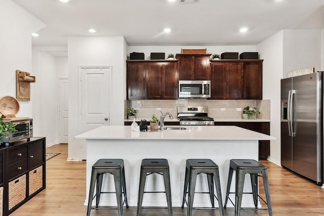 kitchen featuring appliances with stainless steel finishes, a kitchen breakfast bar, a kitchen island with sink, and light hardwood / wood-style flooring