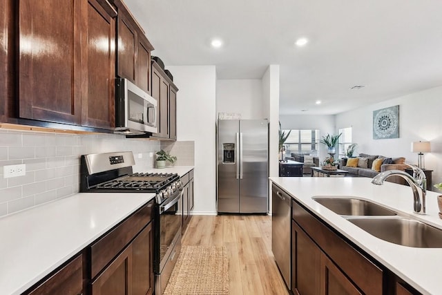 kitchen featuring sink, appliances with stainless steel finishes, dark brown cabinets, tasteful backsplash, and light wood-type flooring