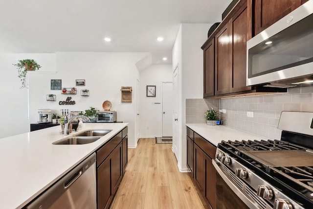 kitchen with dark brown cabinetry, sink, tasteful backsplash, stainless steel appliances, and light hardwood / wood-style floors