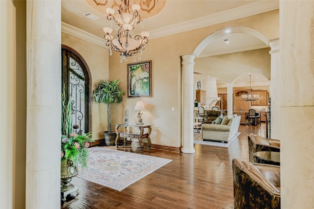 entryway with hardwood / wood-style floors, crown molding, decorative columns, and a chandelier