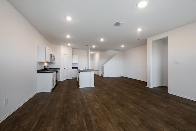 kitchen with dark wood-style flooring, dark countertops, appliances with stainless steel finishes, open floor plan, and an island with sink