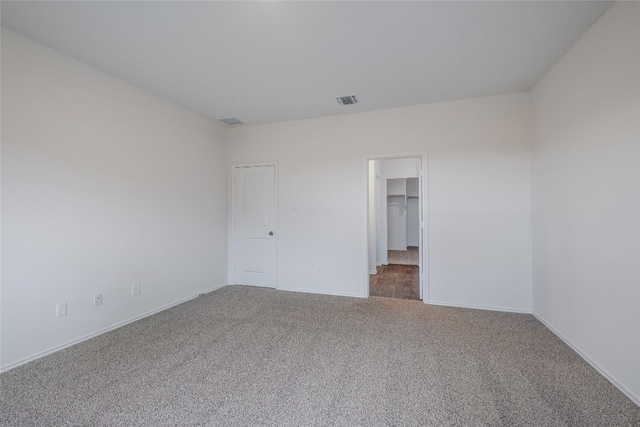 unfurnished bedroom with a spacious closet, carpet, visible vents, and baseboards