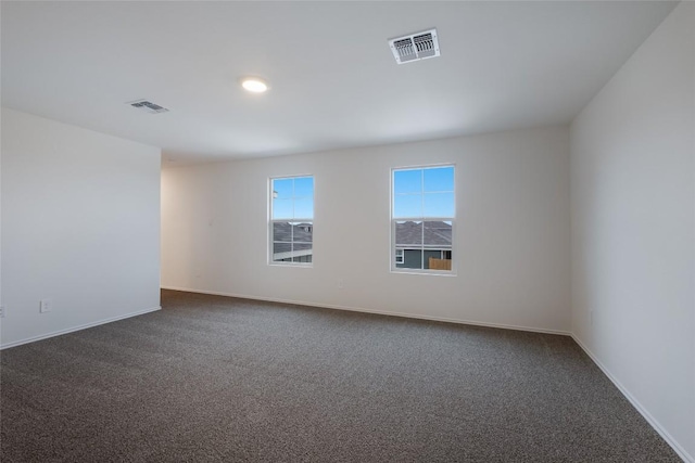 spare room featuring baseboards, visible vents, and dark carpet