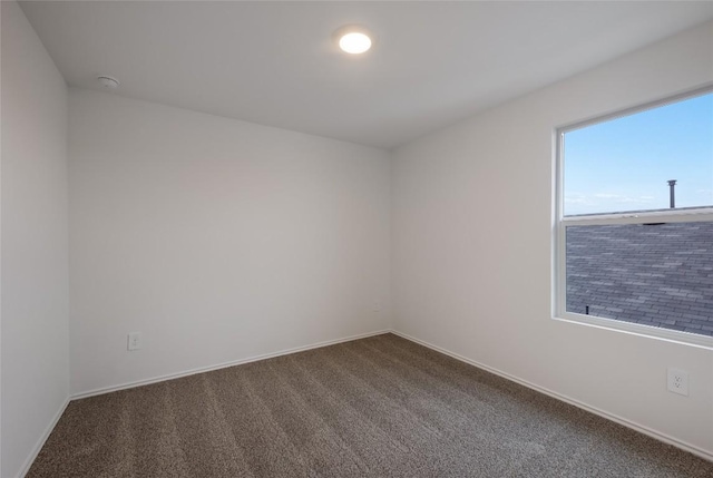 unfurnished room with baseboards and dark colored carpet