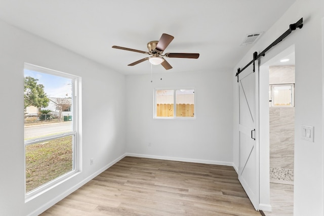 empty room with ceiling fan, a barn door, and light hardwood / wood-style floors