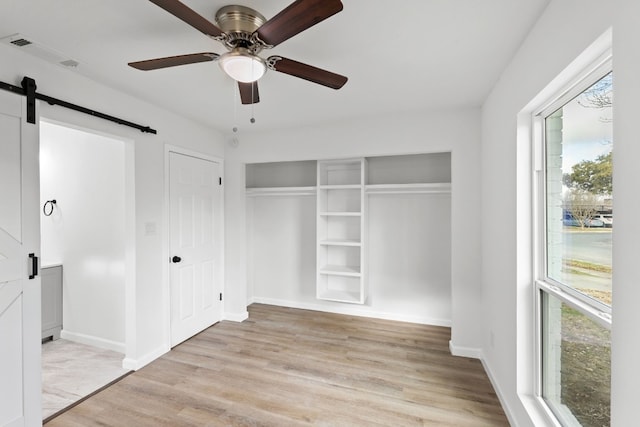 unfurnished bedroom with a barn door, ceiling fan, and light wood-type flooring