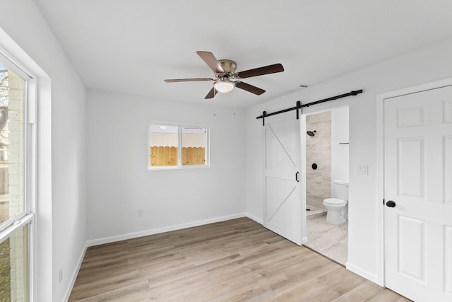 unfurnished bedroom featuring ensuite bathroom, a barn door, ceiling fan, and light hardwood / wood-style floors