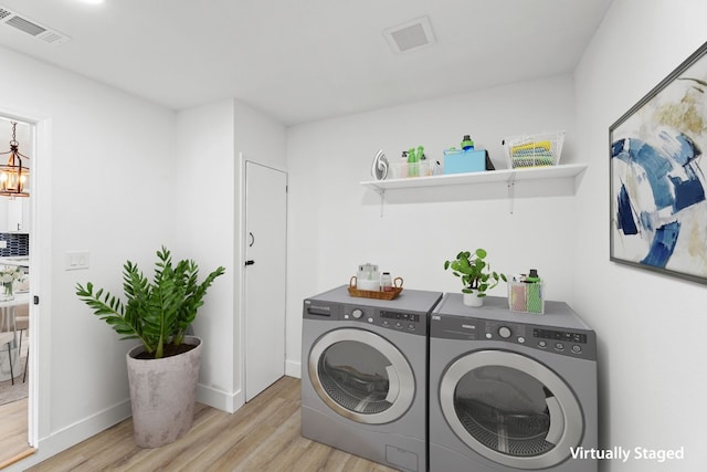 laundry room featuring light hardwood / wood-style flooring, washing machine and dryer, and a chandelier