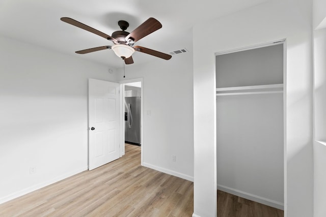 unfurnished bedroom featuring a closet, light hardwood / wood-style flooring, ceiling fan, and stainless steel fridge with ice dispenser