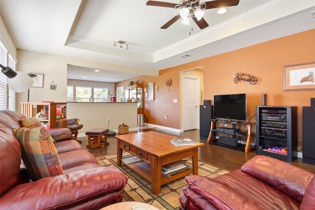 living room with crown molding, rail lighting, a raised ceiling, and hardwood / wood-style floors