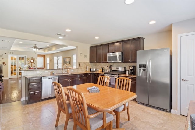 kitchen with sink, dark brown cabinets, stainless steel appliances, a raised ceiling, and kitchen peninsula