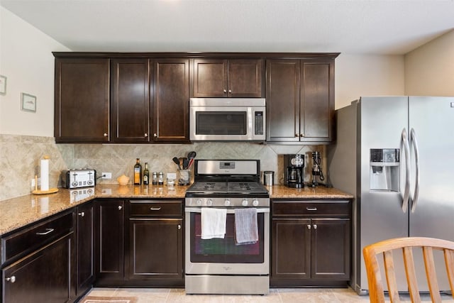 kitchen featuring stainless steel appliances, light stone countertops, and dark brown cabinets