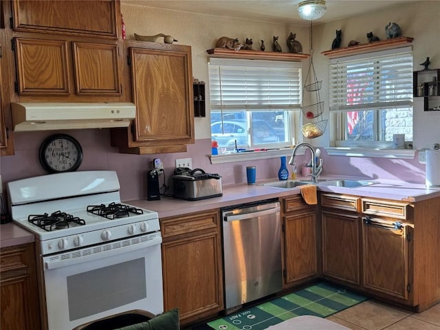 kitchen featuring under cabinet range hood, white range with gas stovetop, a sink, light countertops, and stainless steel dishwasher